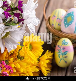 Bunte weiße und gelbe Gänseblümchen mit Ostereiern und Korb im Hintergrund Stockfoto