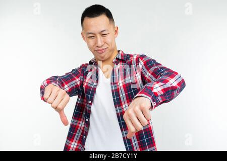 Asian man in einem karierten Hemd weit offen zeigt unartigen Finger unten auf einem isolierten weißen Studiohintergrund Stockfoto