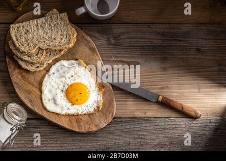 Frittiertes Bio-Ei sonnig mit Salz und Pfeffer auf einem Teller mit Vollkornbrot auf der Seite, auf einer Holzschnittplatte Draufsicht. Stockfoto