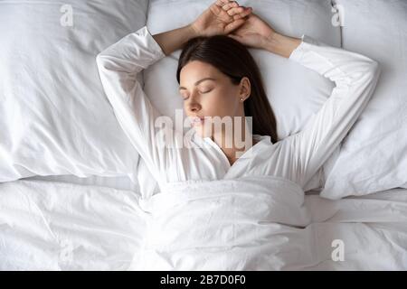 Ruhige junge Brunette-Frau, die im komfortablen Bett schläft. Stockfoto