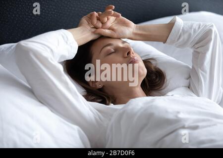 Betonte junge brünette Frau im Bett liegend mit Händen am Kopf Stockfoto
