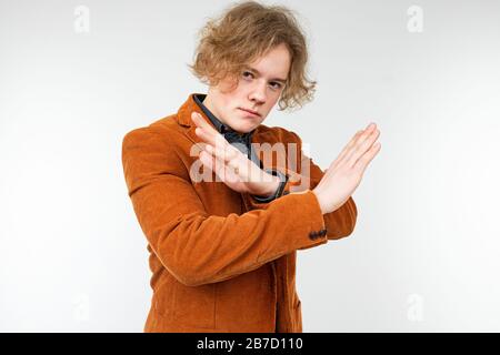 Selbstbewusster, lockig blonder Kerl in einer braunen Jacke, der seine Hände auf einem weißen Studiohintergrund weckt Stockfoto