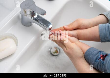 Mutter hilft kleinen Kindern, die Hände über eine weiße Spüle zu waschen Stockfoto