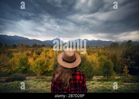 Frau in rot überprüft Hemd und Hut Herbst Wald und Berge Hintergrund betrachten. Reisekonzept. Stockfoto