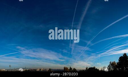 Flugchemtrails über die Bäume in blauem Himmel mit Wolken Stockfoto