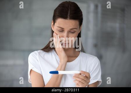 Unglücklich frustrierte junge Frau, die sich einen Plastiktest ansieht. Stockfoto