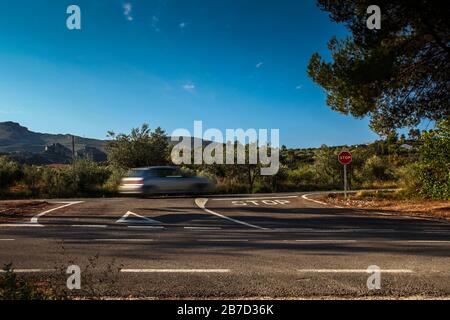 Straßenkreuzung mit Stoppschild und Auto in einer Landstraße Stockfoto