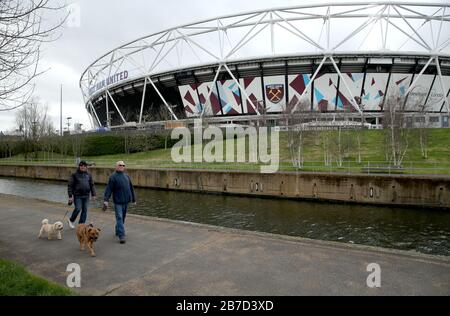 Menschen, die ihre Hunde in der Nähe des London Stadions, dem Heimstadion des West Ham United Football Club, laufen, nachdem am Freitag bekannt gegeben wurde, dass die Premier League alle Spiele bis Samstag, den 4. April 2020, ausgesetzt hat. Stockfoto