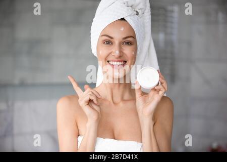 Junge lächelnde Frau in Handtüchern verpackt, die Creme zeigen. Stockfoto