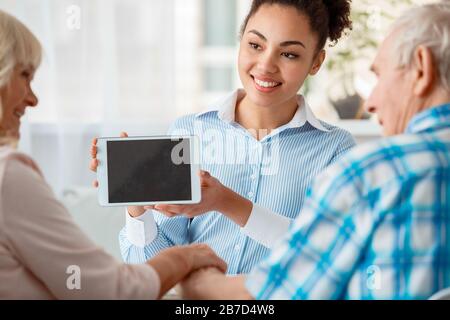 Afrikanische Abstiegsfrau Reisebüro im Büro lächelnd freudig mit Reiseoptionen auf dem digitalen Tablet zum Senioren-Paar Rückansicht Nahaufnahme Stockfoto