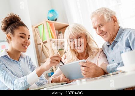Afrikanische Abstiegsfrau Reisebüro im Büro zeigt Reiseoptionen für ältere Paare auf digitalem Tablet lächelnd fröhlich Stockfoto