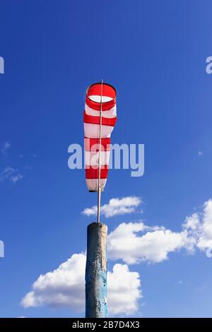 Ein Windbock auf dem Fahnenmast gegen blau bewölkt Himmel weiß und rot gestreifte konische Textilröhre Stockfoto