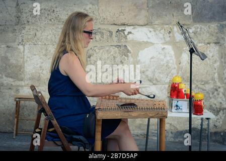 Eine Dame, die ein Hackbrett, ein Percussion Saiteninstrument, spielt, von der Kathedrale von Siena (Duomo di Siena) auf der Piazza del Duomo, Siena, Toskana. Stockfoto