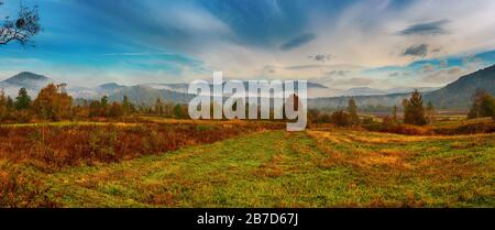 Ländliche nebligen Herbst Landschaft mit roten Bäume und Wolken. Saisonale Herbst stille Stimmung. Panoramablick. Stockfoto