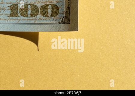 Stück 100-Dollar-Rechnung in der linken oberen Ecke auf goldgelbem Hintergrund. Konzeptionelles Foto, minimalistisches Design Stockfoto