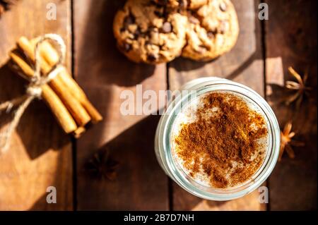 Blick auf eine Tasse heißer, türkischer Sahlep auf einer rustikalen Oberfläche mit Zimtstöcken und Plätzchen Stockfoto