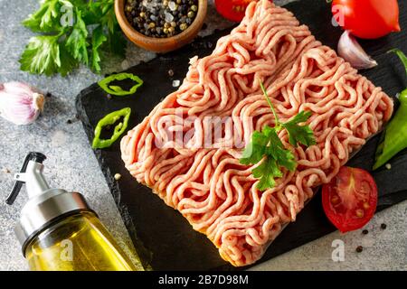 Mince. Frisches rohes Hackfleisch auf dem Schneidbrett und Zutaten zum Kochen auf einem Stein- oder Schiefertisch. Stockfoto