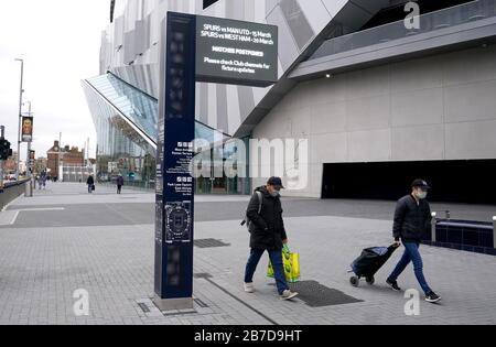 Menschen, die Schutzmasken tragen, gehen am Tottenham Hotspur Stadium, der Heimat des Tottenham Hotspur Football Club, vorbei, nachdem am Freitag bekannt gegeben wurde, dass die Premier League alle Spiele bis Samstag, den 4. April 2020 ausgesetzt hat. Stockfoto