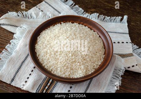 Trockene Reiskörner in einer Tonschale. Braune Schüssel oben auf einem Leintuch. Traditionelle Küche. Draufsicht in einem Winkel. Selektiver Fokus. Nahaufnahme. Stockfoto