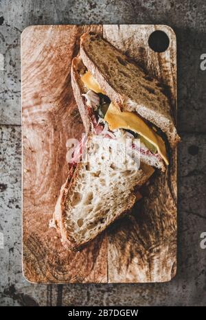 Flat-lay von großen Ruben pastrami Sandwichscheiben in Sauerteigbrot mit Käse, pastrami, Sauerkraut und eingepickte Gurke auf dem Holzbrett Stockfoto