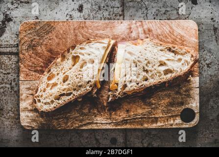 Flat-lay von großen Ruben pastrami Sandwich in Sauerteig Brot mit Käse, pastrami, Sauerkraut und eingepickte Gurke auf dem servieren von Holzbrett über Rough Stockfoto