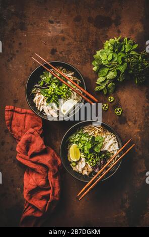 Mittagessen mit asiatischer Küche. Flat-lay von vietnamesischem Reis Nudelhuhnsuppe Pho Ga mit Cilantro, Sojasprossen, frischen Grüns, Kalk in schwarzen Schüsseln mit Schopfsti Stockfoto