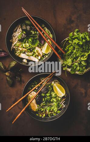 Trendige asiatische Küche Mittagessen. Flat-lay aus vietnamesischem traditionellen Reisnudel und Hühnersuppe Pho Ga mit frischem Cilantro, Sojasprossen, Grüns und Limette i Stockfoto