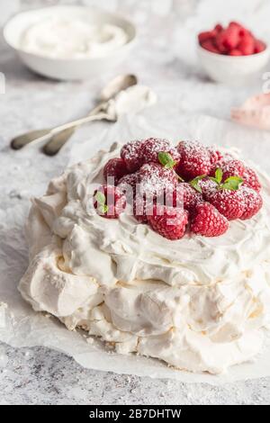 Pavlova Dessert, serviert mit Mascarpon-Creme und frischen Rasbeeren. Mit frischer Minze garniert und mit Puderzucker bestäubt, Stockfoto