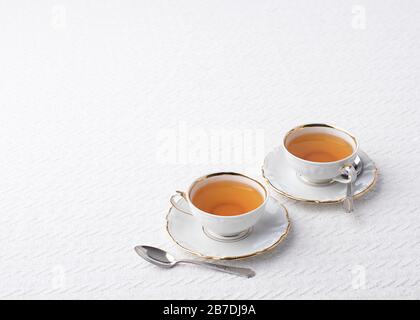 Weiße china-teetassen mit goldenem Besatz mit einem Touch Textur in der weißen Tischdecke, die einen Hintergrund mit Platz für Text bildet Stockfoto