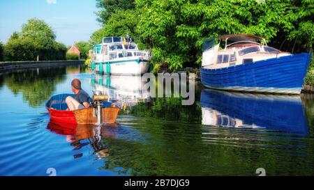 Schlauchboot mit Seagull Außenbordmotor, der entlang des Flusses Soar an vertäuten Booten vorbeifährt, in Leicestershire, England, Großbritannien, Großbritannien, Stockfoto