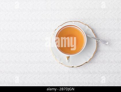 Eine Tasse heißen Tee in einem eleganten weißen china-becher und Untertasse mit Goldbesatz von oben auf einem weißen Tischtuch Stockfoto