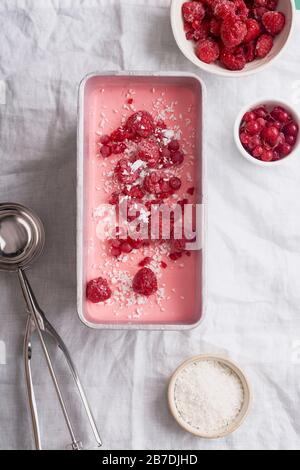 Rosa Eiscreme mit Himbeeren und roten Korinten auf weißem Leinentisch. Overhead-Ansicht Stockfoto