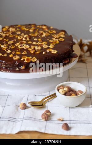 Veganer Brownie-Kuchen mit Haselnüssen und gesalzenem Karamell n weißem Kakestand Stockfoto