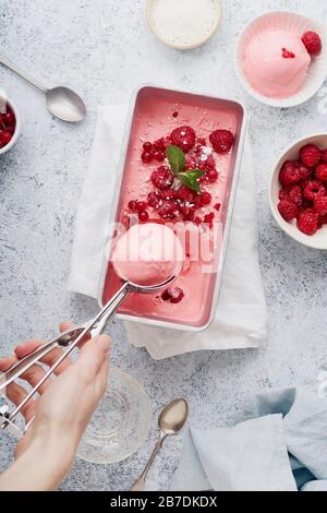 Weibliche Hand, pinkfarbene Eiscreme mit Himbeeren, Minze und roten Korinten. Draufsicht Stockfoto