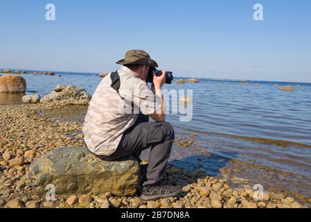 LENINGRADER REGION, RUSSLAND - 06. JUNI 2019: Ein männlicher Tourist, der an einem sonnigen Junitag auf einem Steinbild den finnischen Meerbusen fotografiert Stockfoto