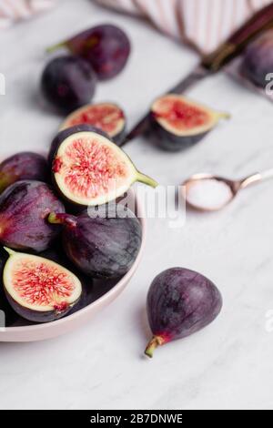 Eine Schale voller und halbierter lila Feigen auf einer weißen Marmorunterseite. Stockfoto