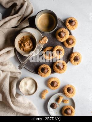Erdnussbutter in einer Quetschschüssel auf einer dunkelgrauen Platte, umgeben von Keksen aus Schokolade Stockfoto