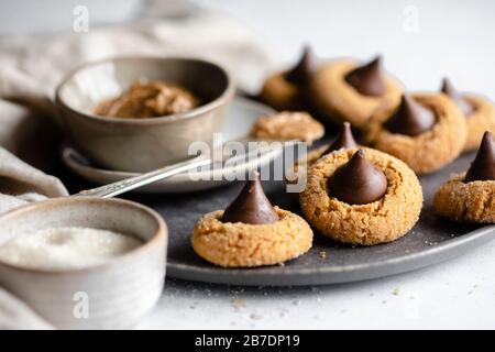 Erdnussbutter in einer Quetschschüssel auf einer dunkelgrauen Platte, umgeben von Keksen aus Schokolade Stockfoto