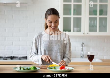 Lächelnde junge Frau, die in der Küche Gemüse für Salat schneidet Stockfoto