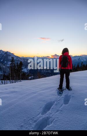 Abenteuerliches Mädchen Schneeschuhwandern im Schnee auf einem Berg bei einem lebhaften und farbenfrohen Winter-Sonnenuntergang. Aufgenommen auf Anif Peak, Squamish, British Colum Stockfoto