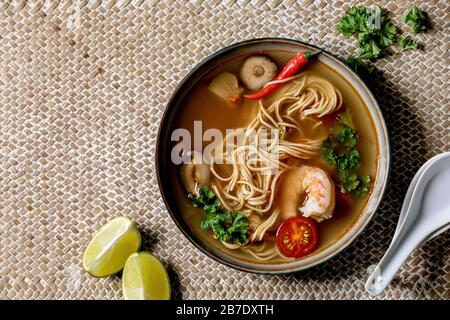 Asiatische würzige Nudeln Suppe mit Shiitake-Champignons und Garnelen, Zutaten oben auf Strohfellernte als Hintergrund. Flaches Layout, Platz. Asiatisches Dinn Stockfoto