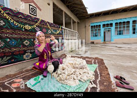 Usbekische Frau in lokaler Kleidung, die die Wolle von Hand spinnt, in Rishtan, Usbekistan. Stockfoto