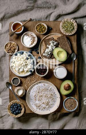 Gesundes Frühstück. Verschiedene Frühstücksgerichte Weizen, Joghurt, Kefir, Hüttenkäse, Avocado, Roggenbrot, Samen, Nüsse und Beeren im Keramiksortiment Stockfoto