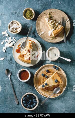 Käsekuchen mit verschiedenen Belägen auf Keramikplatten und verschiedene Soßen in Keramikschalen über blauem Texturhintergrund. Flaches Layout, Platz Stockfoto