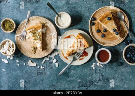 Käsekuchen mit verschiedenen Belägen auf Keramikplatten und verschiedene Soßen in Keramikschalen über blauem Texturhintergrund. Flaches Layout, Platz Stockfoto