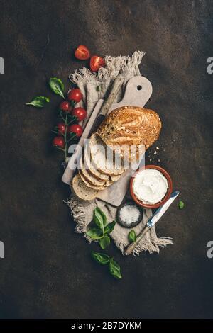 Zutaten für gesunde hausgemachte Sandwiches. Vollkornbrot, Frischkäse, Tomaten und Basilikum auf rustikalem Hintergrund. Gesundes Esskonzept. Flat la Stockfoto