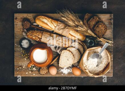 Verschiedene Brotselektion und Backzutaten flach gelegt. Draufsicht auf Rye, Weizen und mehrkörnige rustikale Brotsorten über rustikalen Hintergrund Stockfoto