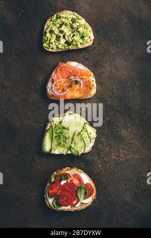 Verschiedene Sandwiches zum Frühstück, Snacks, Vorspeisen - Avocado-Püree, Mozzarella, Tomaten, Basilikum, Frischkäse, Räucherlachs, rote Zwiebel, Gurke Stockfoto