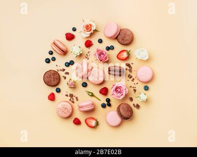 Runde Komposition mit französischen Makronen, Blumen und Beeren auf cremefarbenem Hintergrund. Wunderschönes, kreatives Layout mit Pastellmakaronen oder Makronen in t Stockfoto