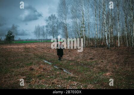 Eine einsame Großmutter, die sich an einem Stock lehnt, geht vom Denkmal aus über das Feld Stockfoto